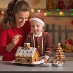 Happy mother and baby decorating christmas cookie house in kitchen
