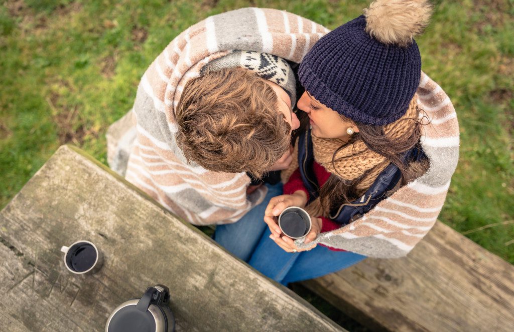 Young couple under blanket with hot drink kissing outdoors